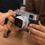 Beginner photographer kneeling with mirrorless camera at golden hour, demonstrating aperture-priority shooting and using the rule-of-thirds grid overlay on camera